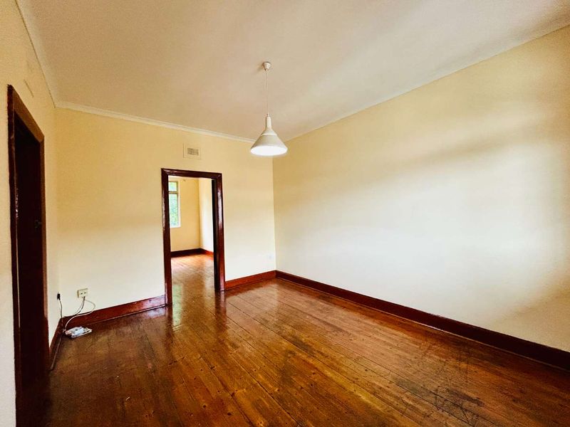 An empty living room featuring original timber flooring, dark wood architraves, and a neutral wall finish, offering a blank canvas for renovation.
