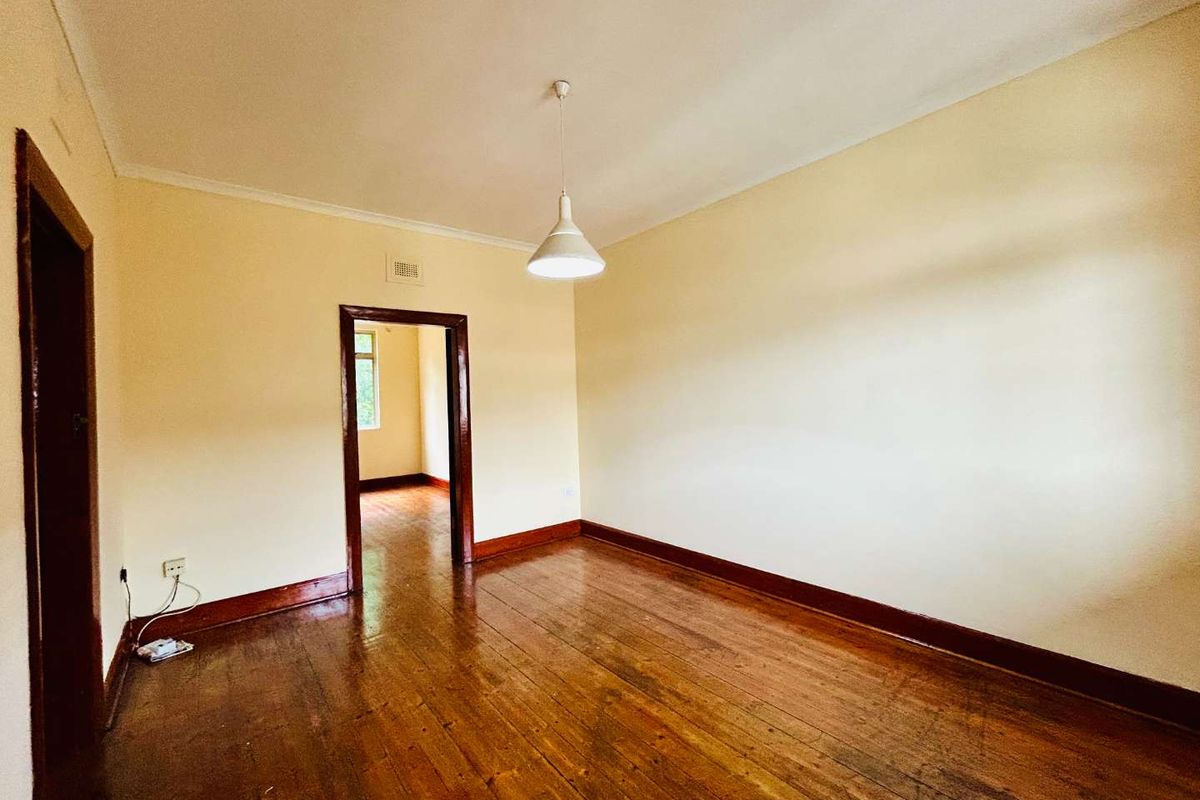 An empty living room featuring original timber flooring, dark wood architraves, and a neutral wall finish, offering a blank canvas for renovation.