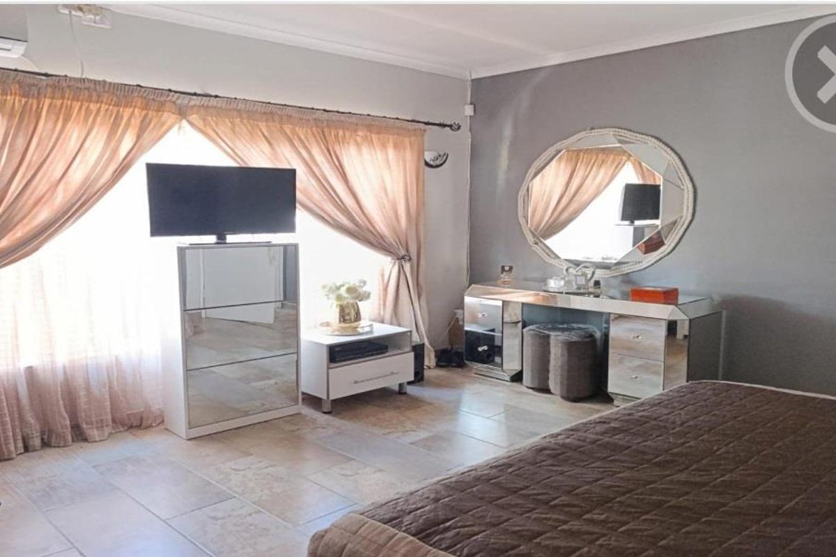 A spacious bedroom featuring tiled flooring, neutral wall finishes, and a wall-mounted air conditioning unit.