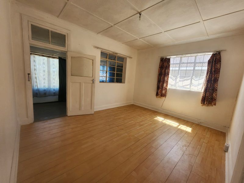 An empty living room featuring laminate flooring, a tiled ceiling, and steel-framed windows, offering a blank canvas for renovation.