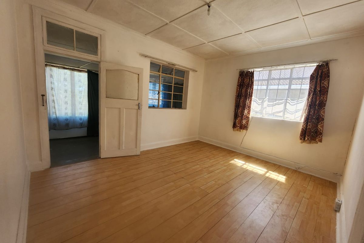 An empty living room featuring laminate flooring, a tiled ceiling, and steel-framed windows, offering a blank canvas for renovation.