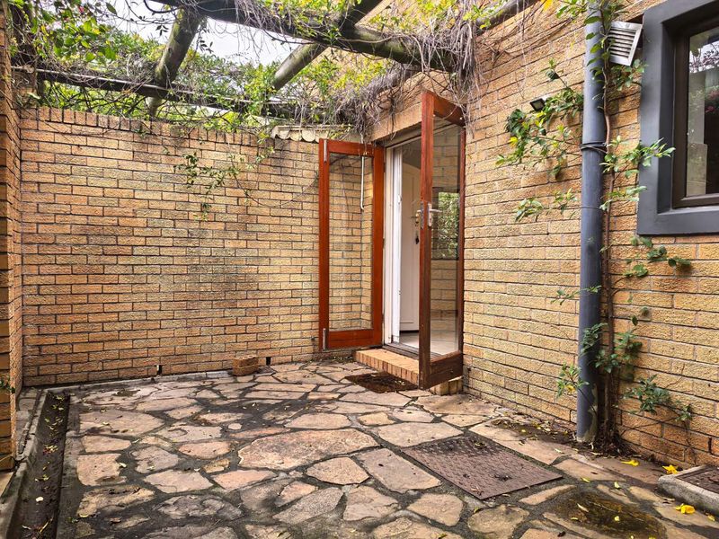 A private outdoor patio area featuring stone paving, a timber pergola, and direct access to the interior through timber-framed glass doors.