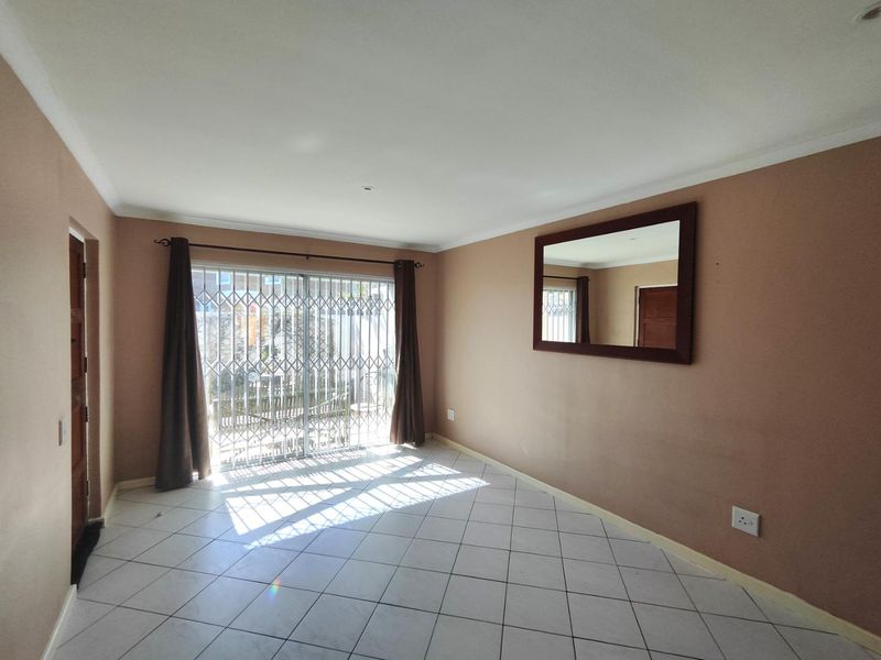 A bright, empty living room featuring tiled flooring and a sliding glass door with a security gate leading to the exterior.