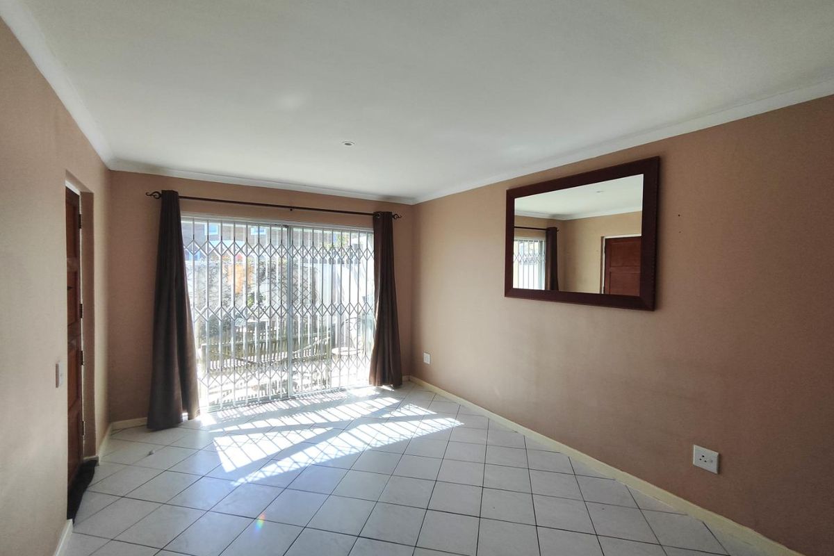 A bright, empty living room featuring tiled flooring and a sliding glass door with a security gate leading to the exterior.