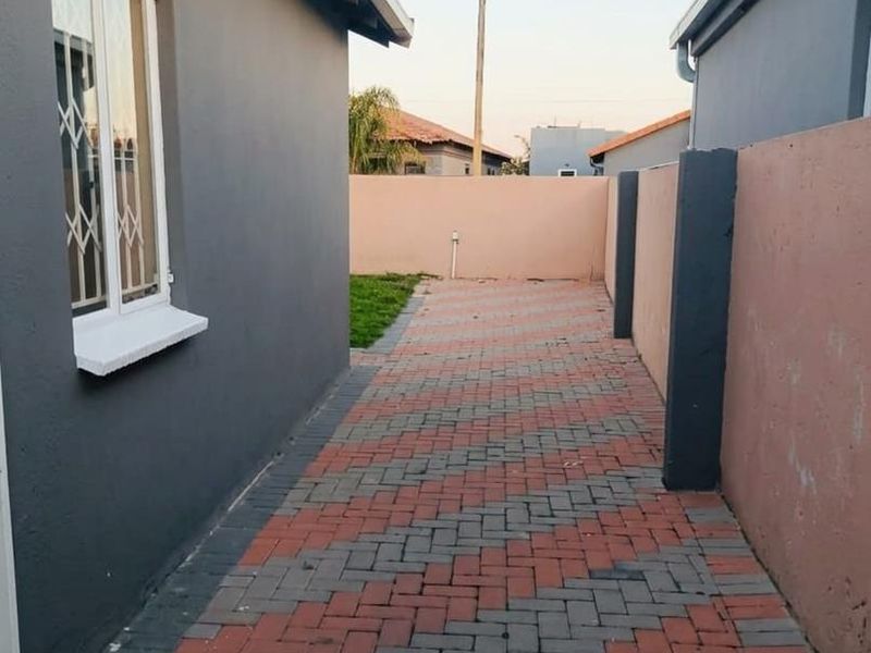 A side passage featuring patterned brick paving, enclosed by a boundary wall and the side elevation of the house with security bars on the window.