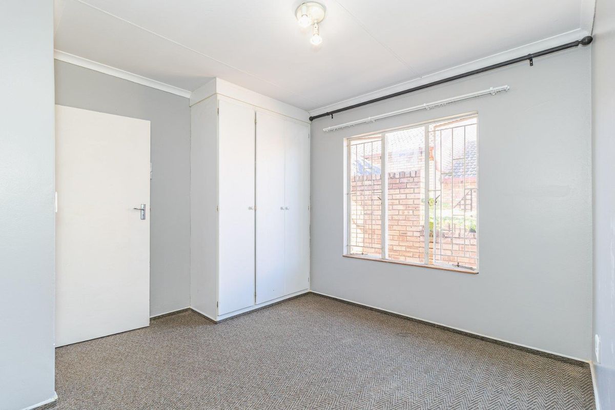 A clean, empty bedroom featuring built-in cupboards, neutral wall paint, and a window with security bars.