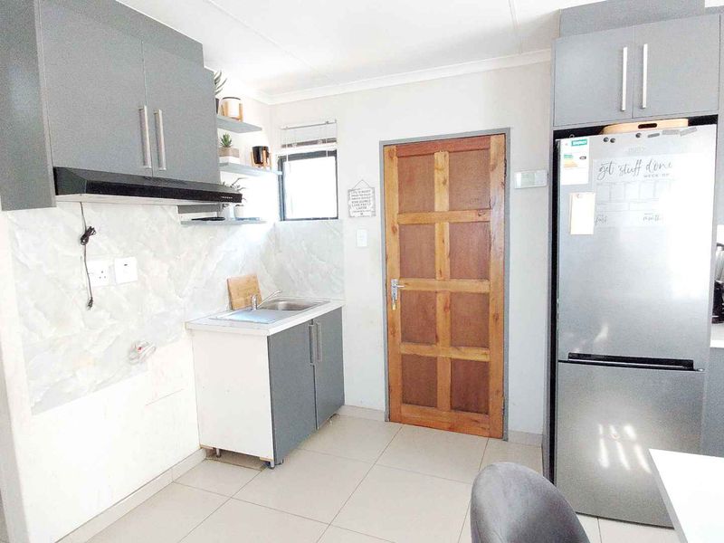 A functional kitchen featuring grey built-in cabinetry, a tiled backsplash, and tiled flooring, with an adjacent doorway leading to a secondary utility space.