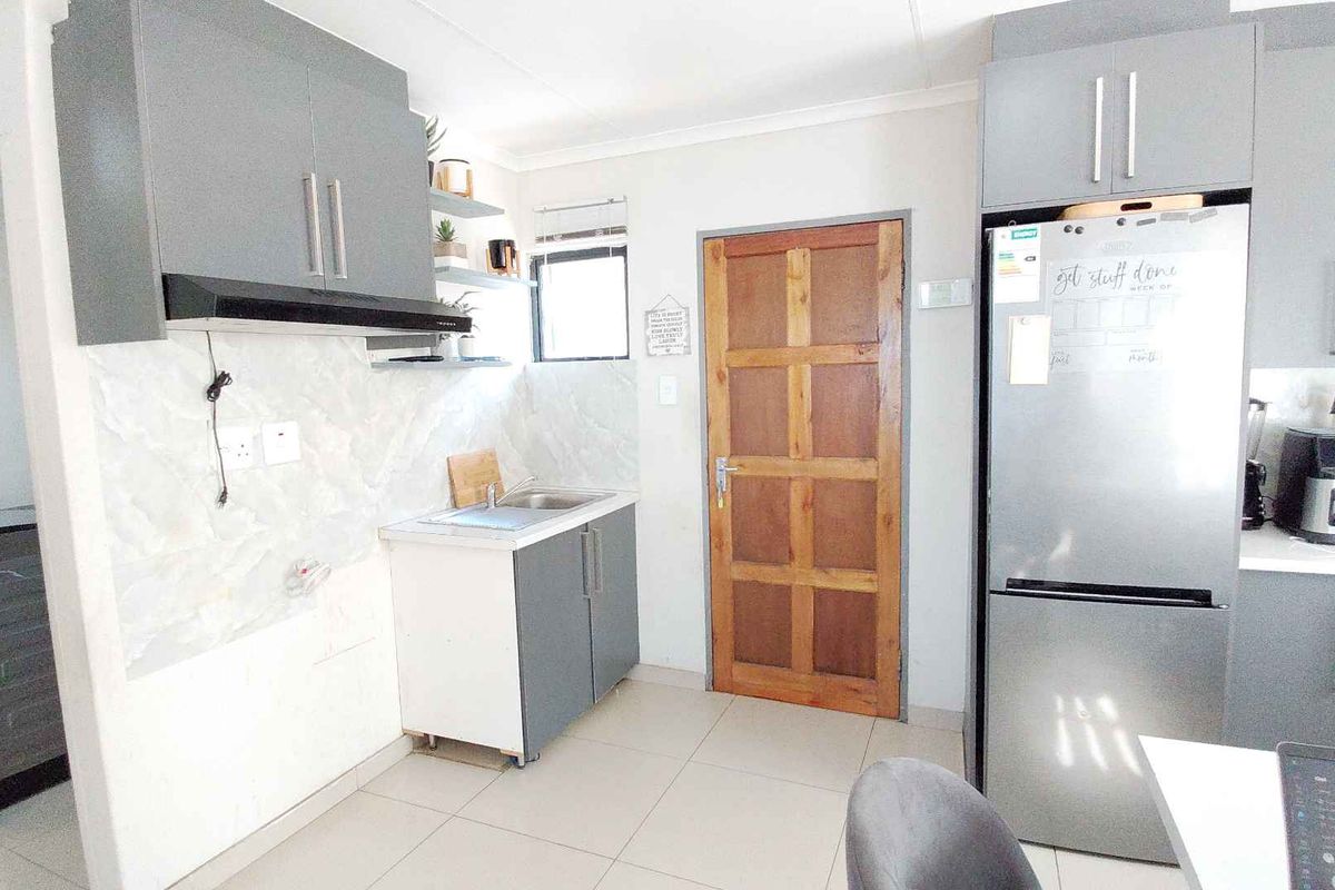 A functional kitchen featuring grey built-in cabinetry, a tiled backsplash, and tiled flooring, with an adjacent doorway leading to a secondary utility space.