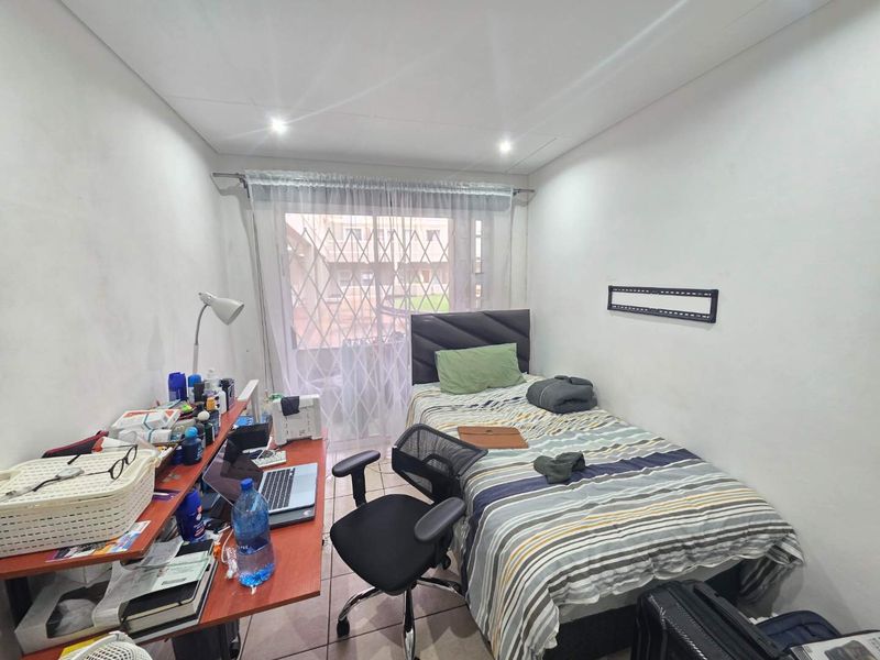 A functional bedroom featuring tiled flooring, recessed downlighting, and a sliding glass door with an integrated security gate providing access to the exterior.