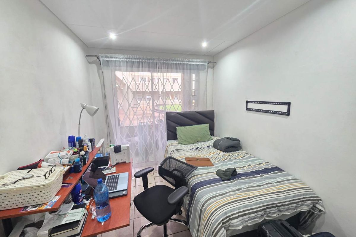 A functional bedroom featuring tiled flooring, recessed downlighting, and a sliding glass door with an integrated security gate providing access to the exterior.