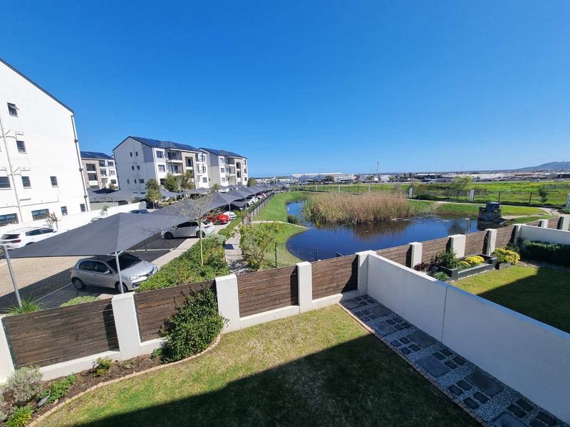 Elevated view overlooking a landscaped garden, small pond, and the apartment complex parking area with shade cloth structures.