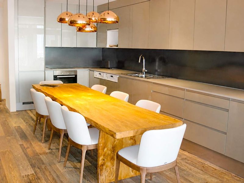 Modern open-plan kitchen featuring sleek high-gloss cabinetry, integrated appliances, and a large central dining area with warm wood-toned flooring.