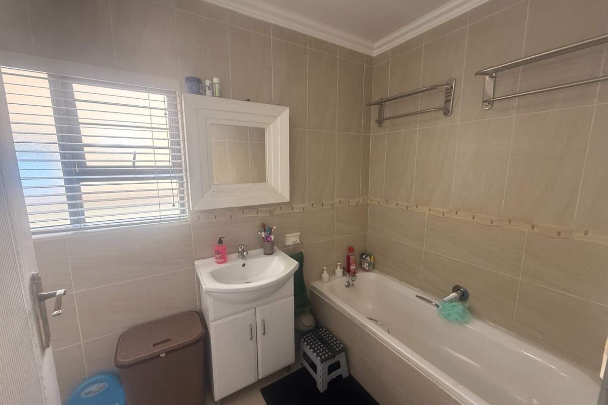 A functional bathroom featuring tiled walls, a vanity cabinet with a basin, and a standard bathtub with wall-mounted towel rails.
