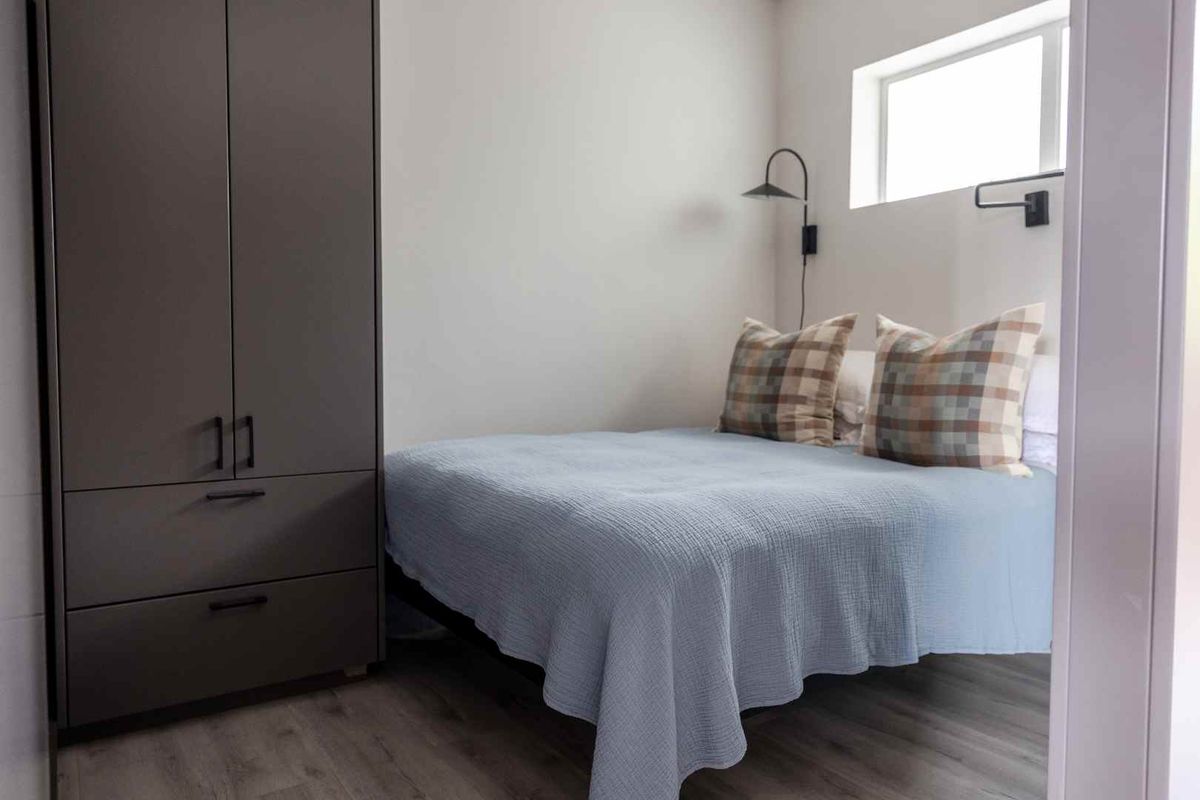 A compact bedroom featuring modern laminate flooring, a built-in wardrobe, and a wall-mounted light fixture.