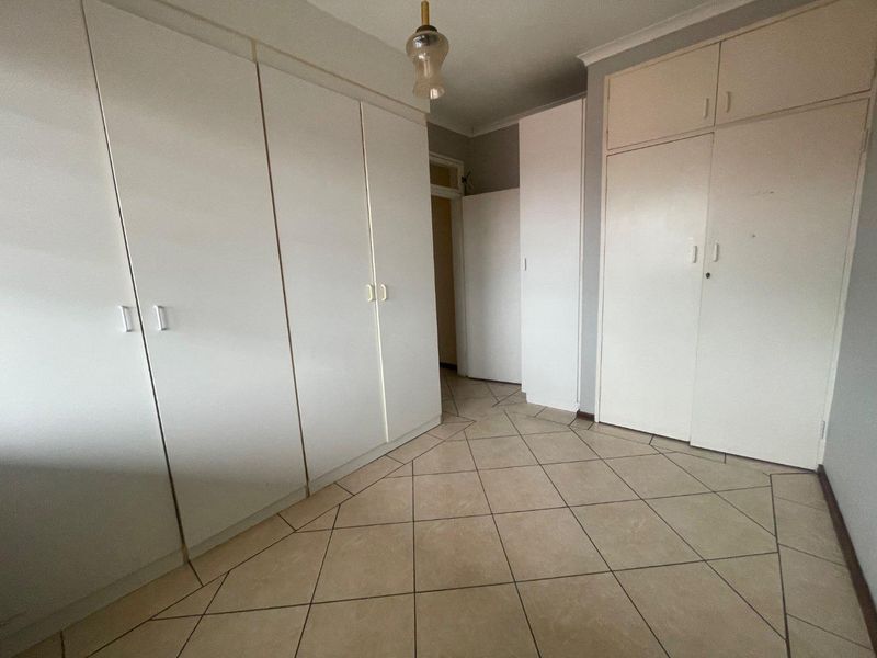 A vacant bedroom featuring extensive built-in cupboard storage and neutral tiled flooring, offering a functional space ready for personalization.