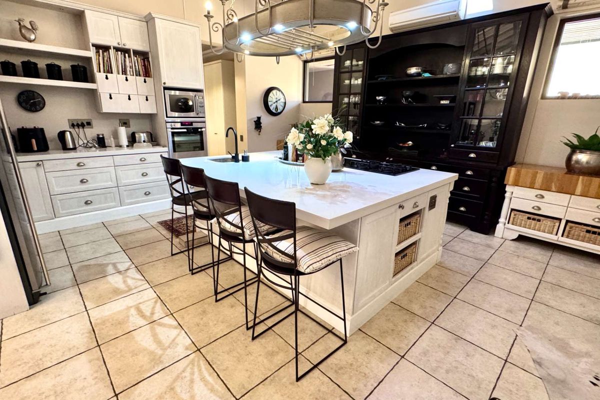 Spacious kitchen featuring a large central island with stone countertops, built-in appliances, extensive cabinetry, and tiled flooring, offering a functional and well-appointed culinary space.