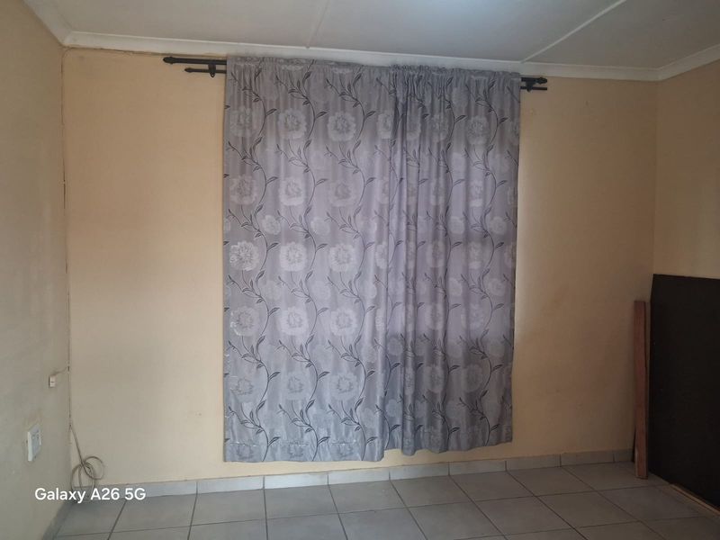 An empty bedroom featuring tiled flooring and a curtain rod, requiring cosmetic updates to the wall finishes.