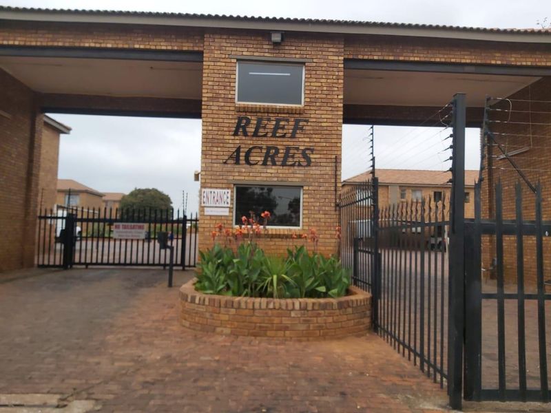The entrance to Reef Acres apartment complex featuring a brick security gatehouse, metal access gates, and electric perimeter fencing.