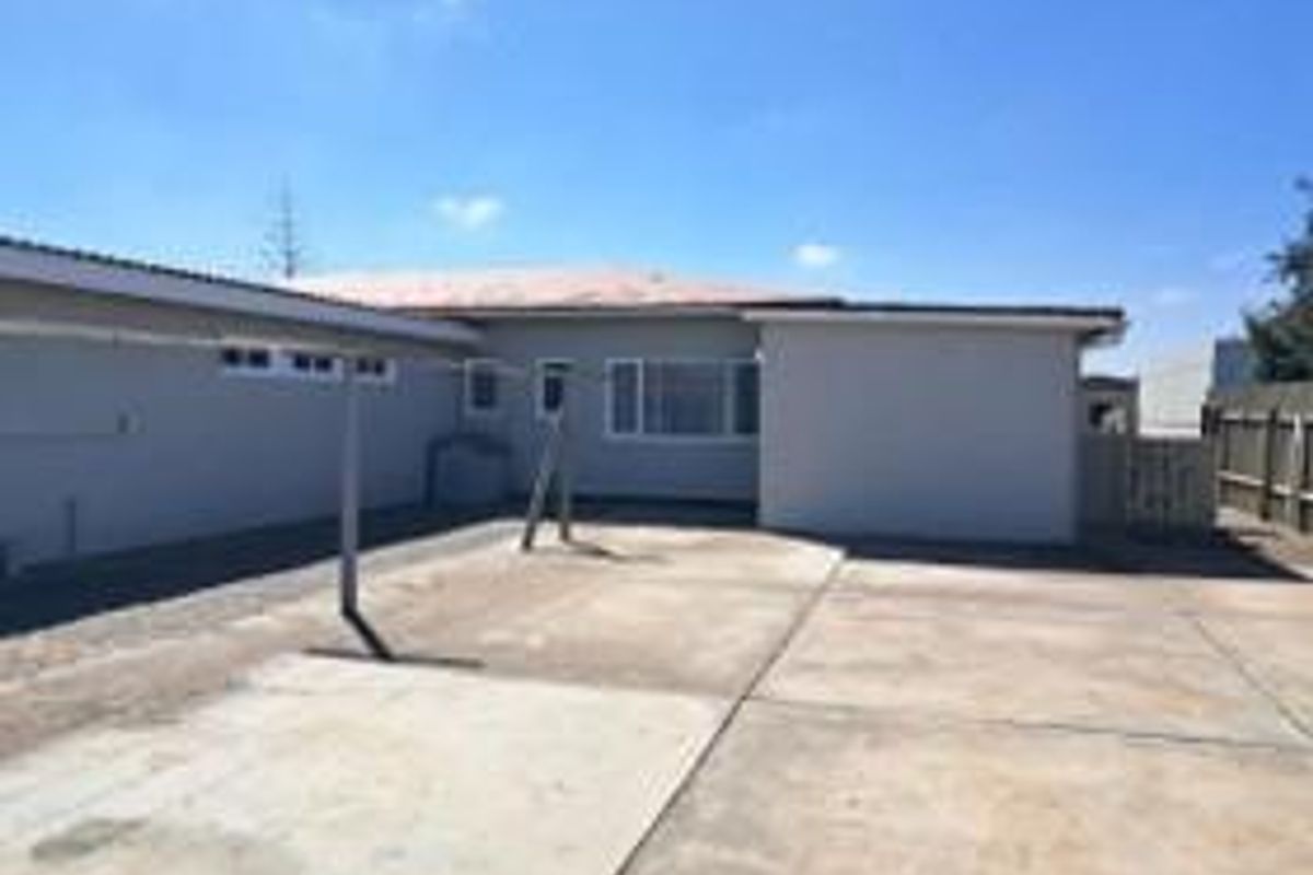 A view of the rear exterior of the house featuring a paved courtyard area and a covered carport structure.