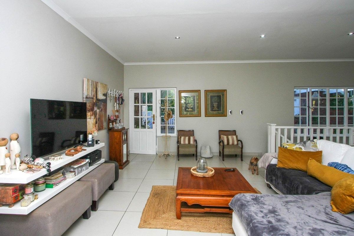 A spacious living room featuring neutral tiled flooring, recessed downlighting, and direct access to an outdoor area through a white timber-framed door.