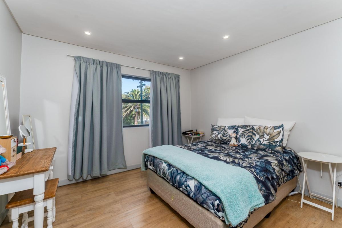 A well-lit bedroom featuring laminate flooring, recessed downlights, and a window with curtains, providing a comfortable and functional living space.