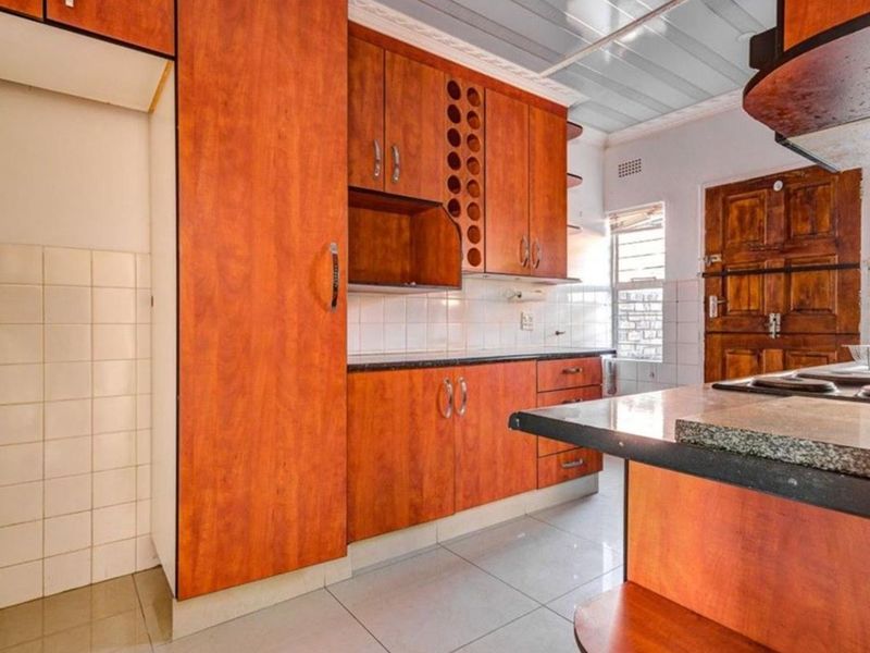 A functional kitchen featuring wood-look laminate cabinetry, granite countertops, tiled backsplash, and tiled flooring, offering a practical layout for culinary activities.