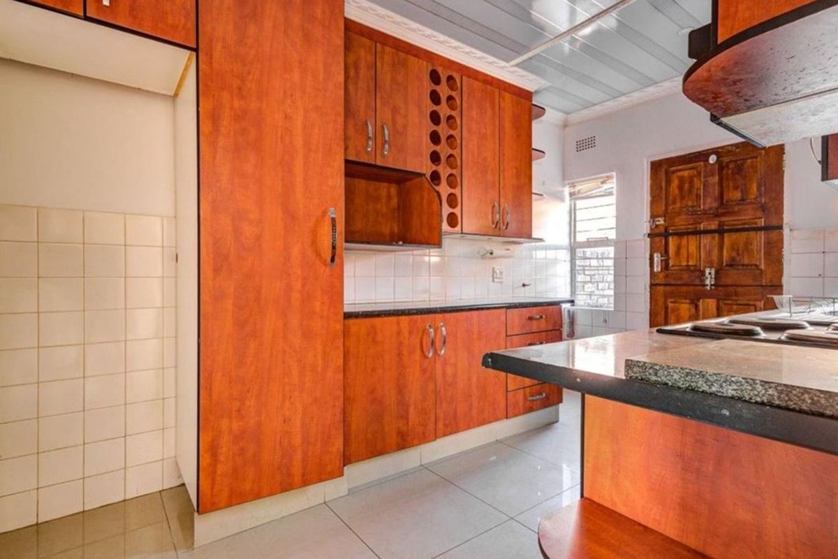 A functional kitchen featuring wood-look laminate cabinetry, granite countertops, tiled backsplash, and tiled flooring, offering a practical layout for culinary activities.