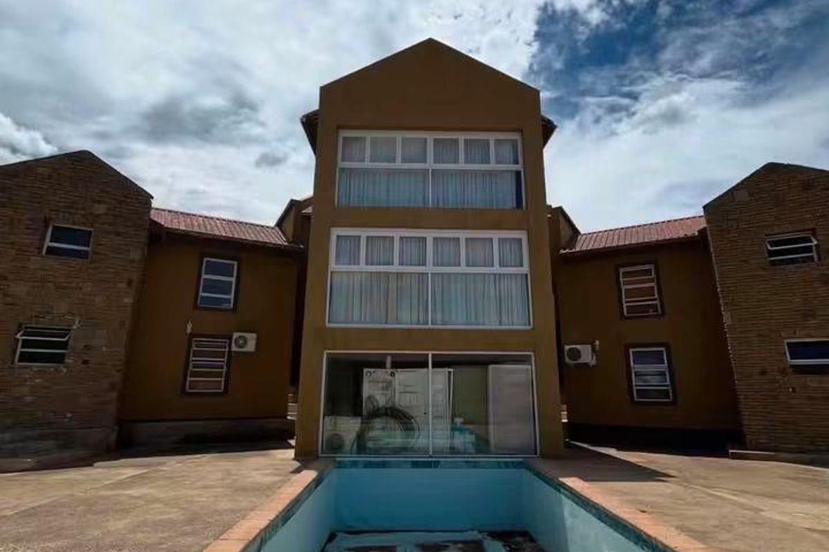 Exterior view of a multi-story residential building featuring a large, empty swimming pool in need of maintenance and repair.