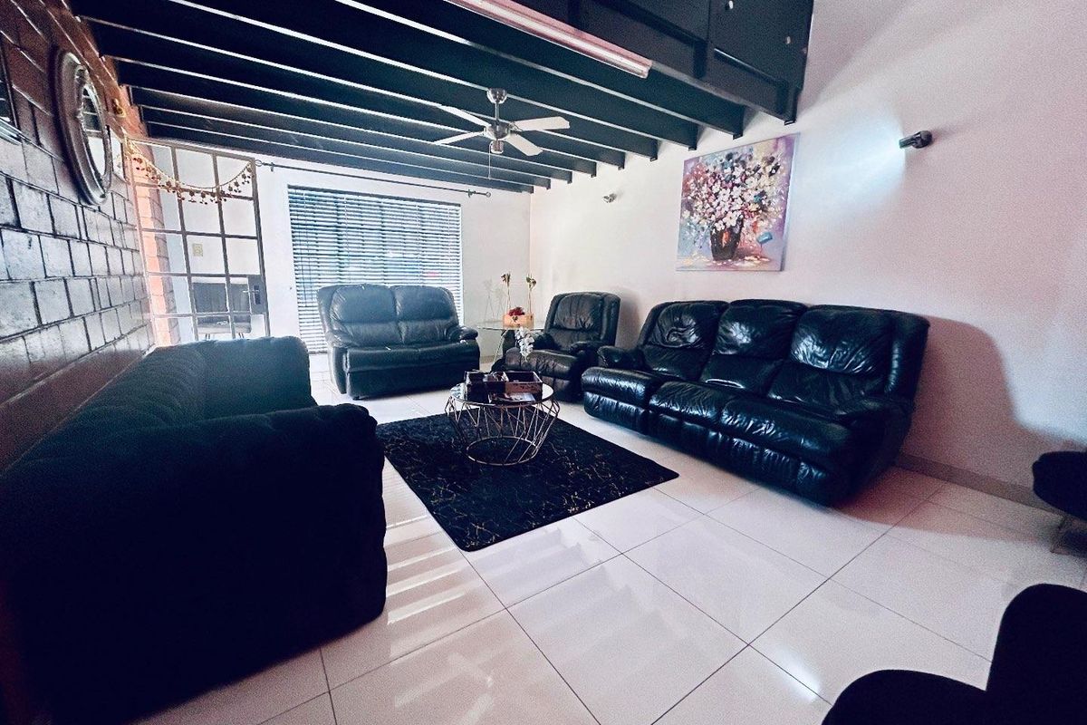Spacious living room featuring high ceilings with exposed beams, large windows with blinds, and polished floor tiles.