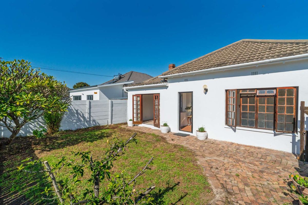 Rear view of the property featuring a brick paved patio, timber framed doors and windows, and a private garden area with boundary walling.