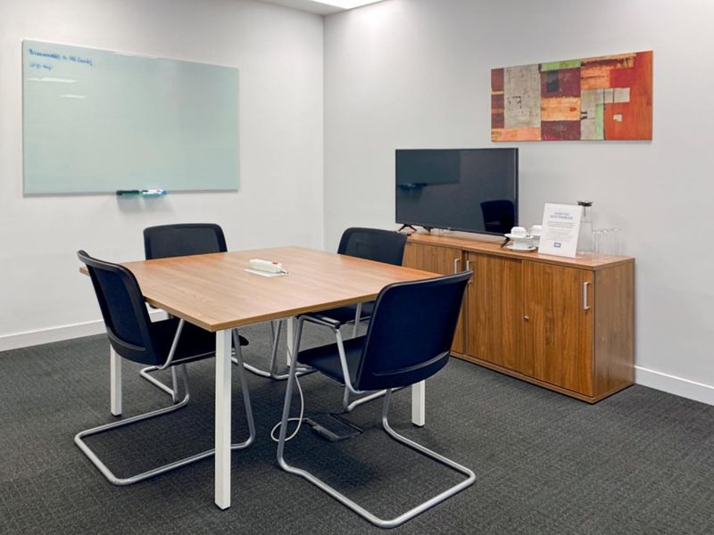 A professional office meeting room featuring a wall-mounted whiteboard and carpeted flooring, suitable for collaborative work and presentations.