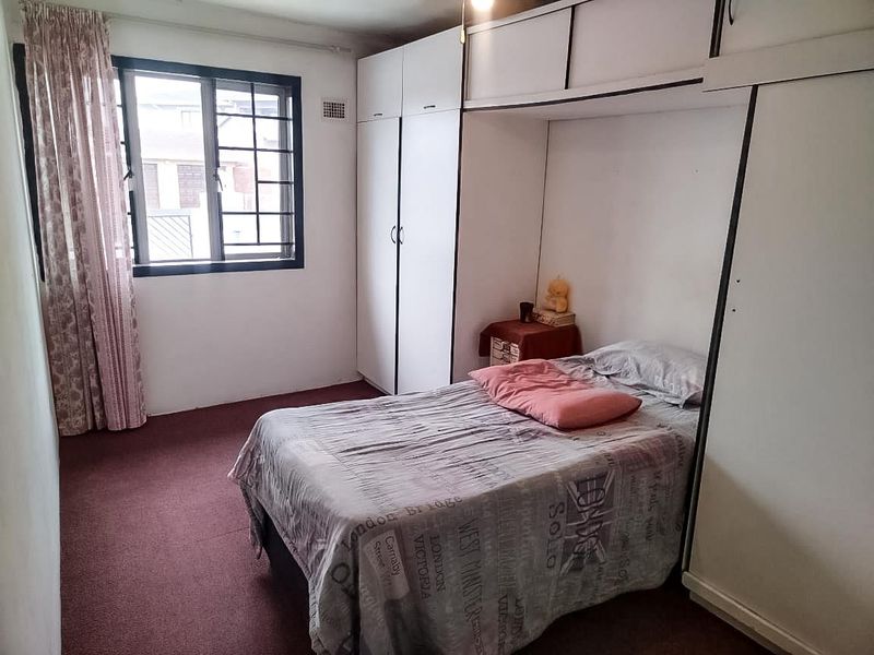 A bedroom featuring built-in cupboards with overhead storage, carpeted flooring, and an aluminium-framed window.