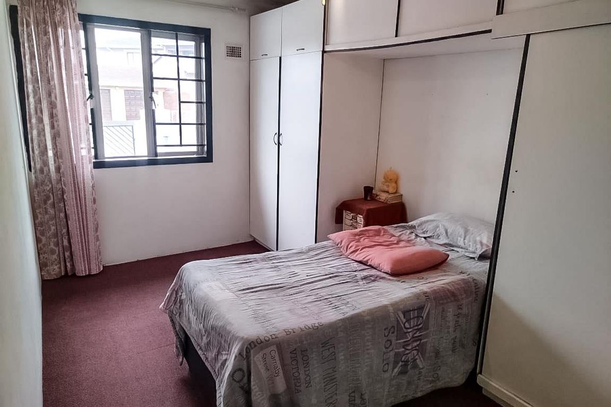 A bedroom featuring built-in cupboards with overhead storage, carpeted flooring, and an aluminium-framed window.