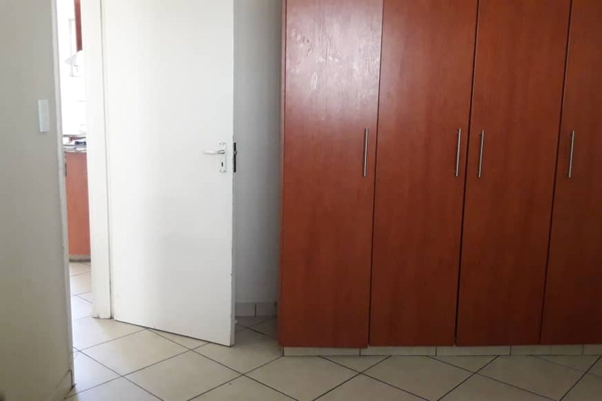 A bedroom featuring built-in wooden cupboards and tiled flooring, with a doorway leading to an adjacent room.