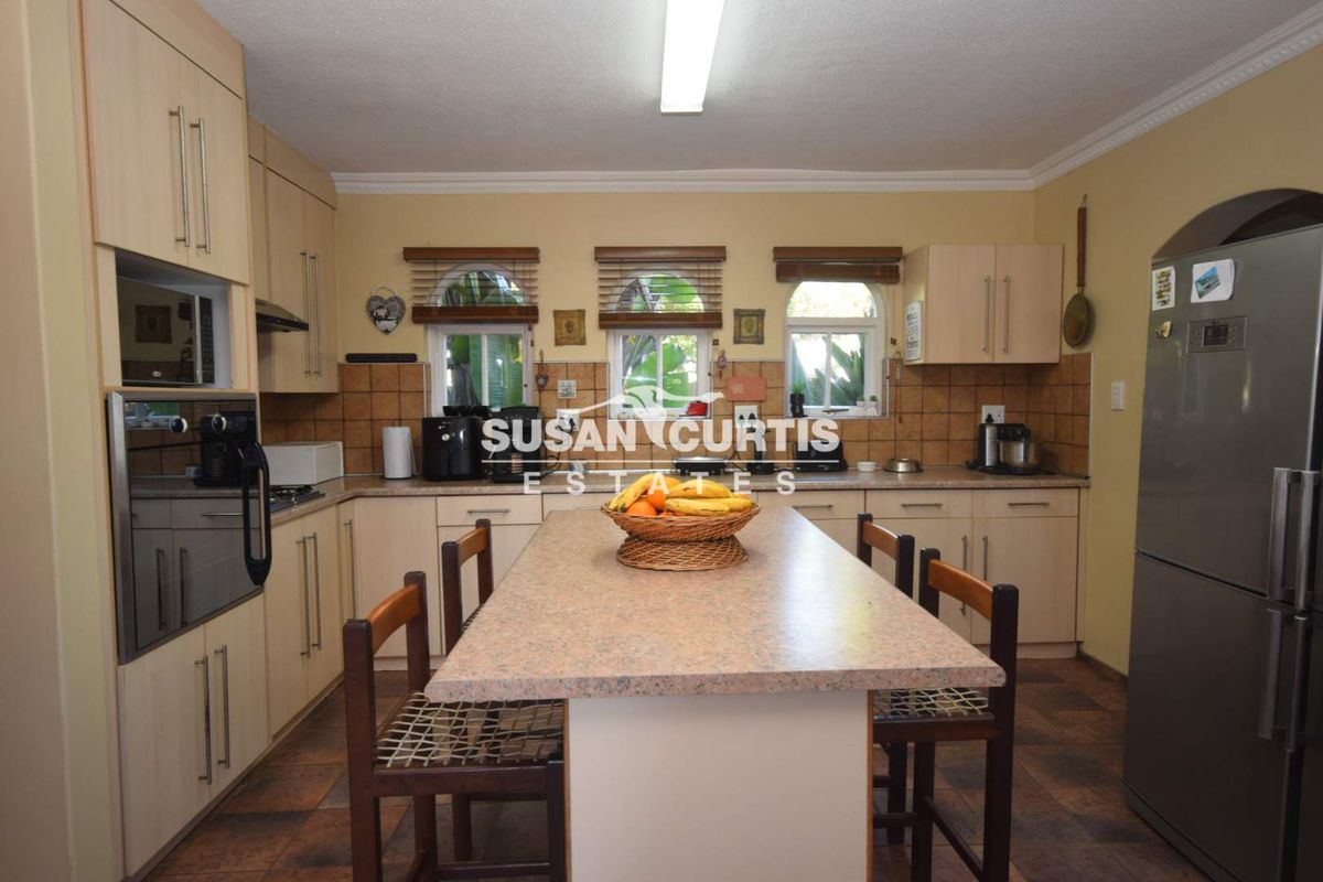 A functional kitchen featuring light-toned cabinetry, a central island with seating, tiled backsplash, and built-in oven, illuminated by natural light from three arched windows.
