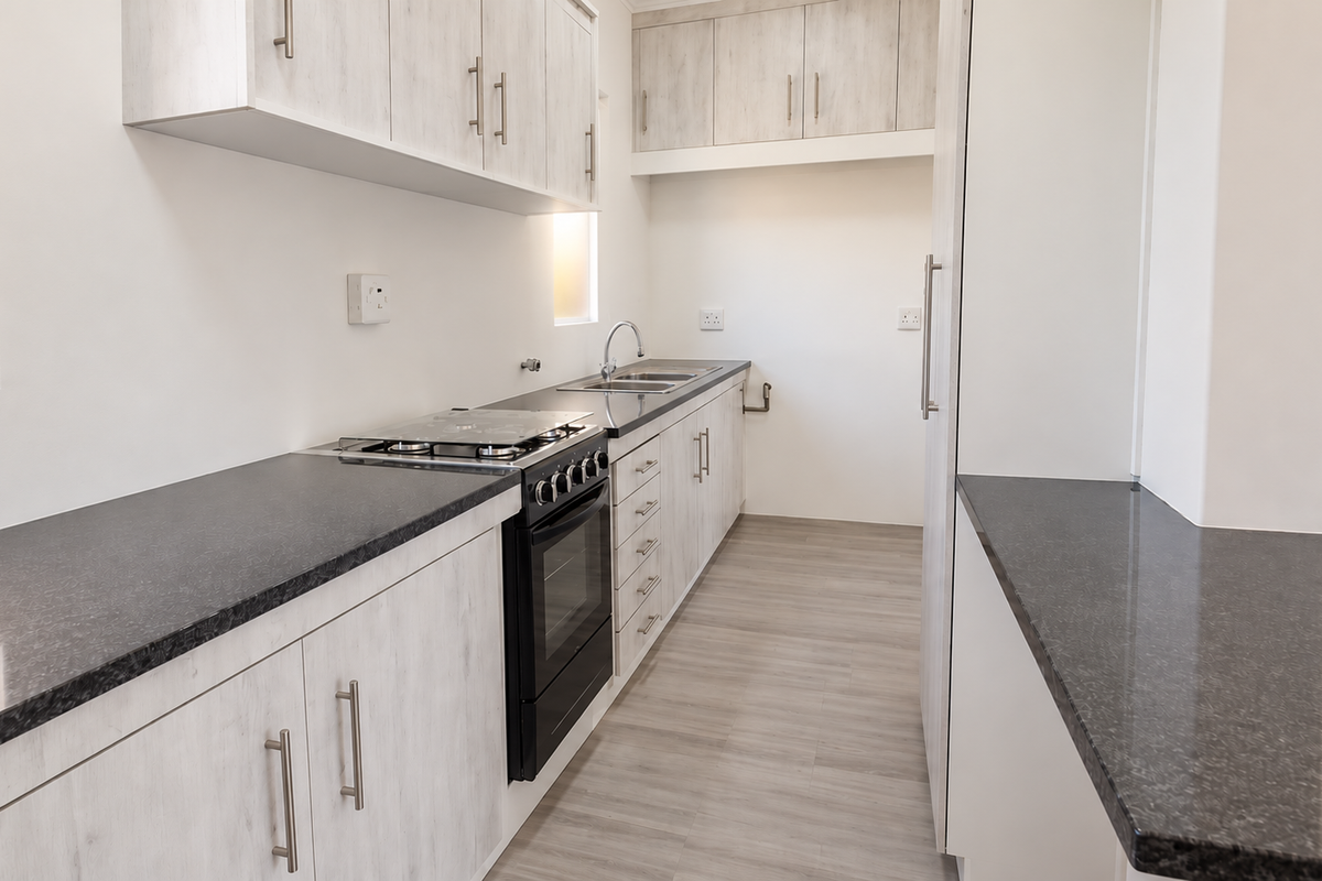 A clean, modern kitchen featuring light wood-grain cabinetry, dark laminate countertops, a built-in oven with gas hob, and durable laminate flooring.