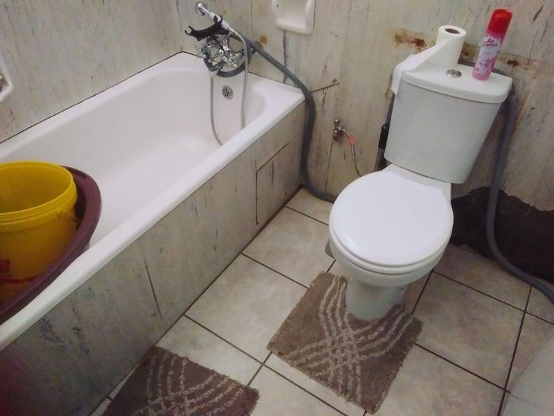 A dated bathroom featuring a standard bathtub and toilet with significant wall surface deterioration and staining, requiring renovation or cosmetic updates.