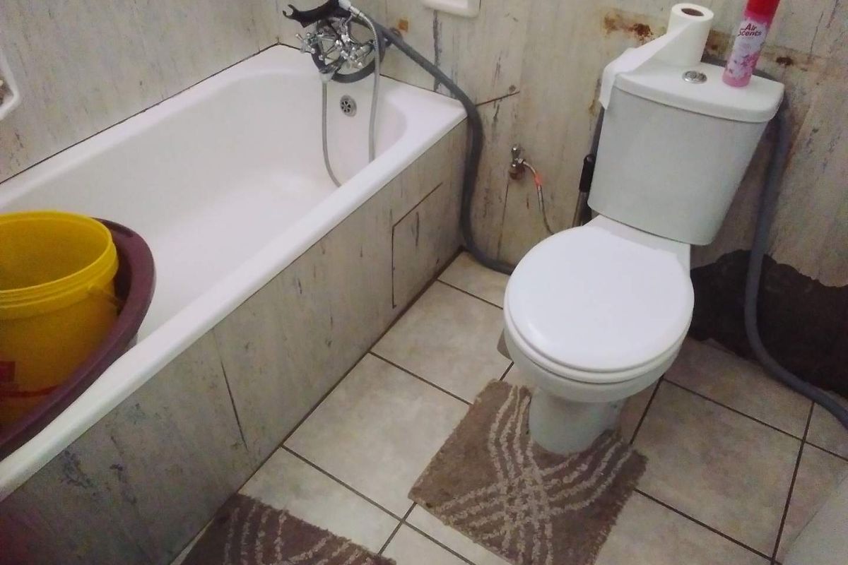 A dated bathroom featuring a standard bathtub and toilet with significant wall surface deterioration and staining, requiring renovation or cosmetic updates.