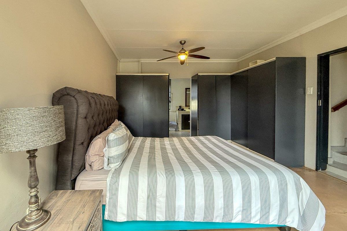 Spacious bedroom featuring built-in dark cabinetry, a central ceiling fan, and direct access to an adjoining bathroom area.