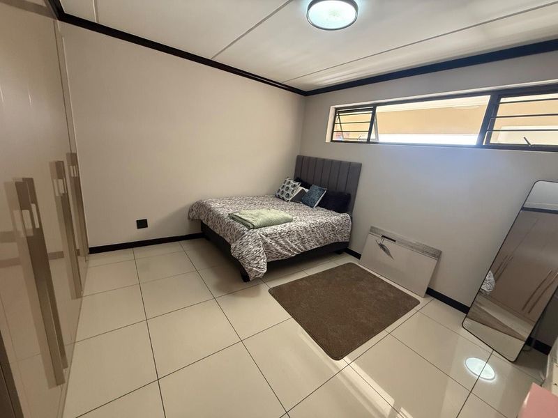 A bedroom featuring tiled flooring, built-in cupboards, and top-hung windows, providing a functional and neutral living space.