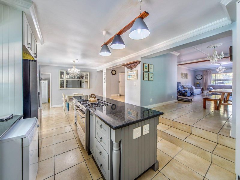 Spacious open-plan kitchen and living area featuring a central island with granite countertops, gas stove, and tiled flooring throughout.