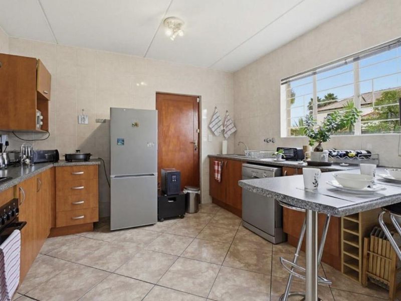 Functional kitchen featuring wood-finish cabinetry, laminate countertops, ceramic tile flooring, and a window with security bars, offering a practical layout for daily use.