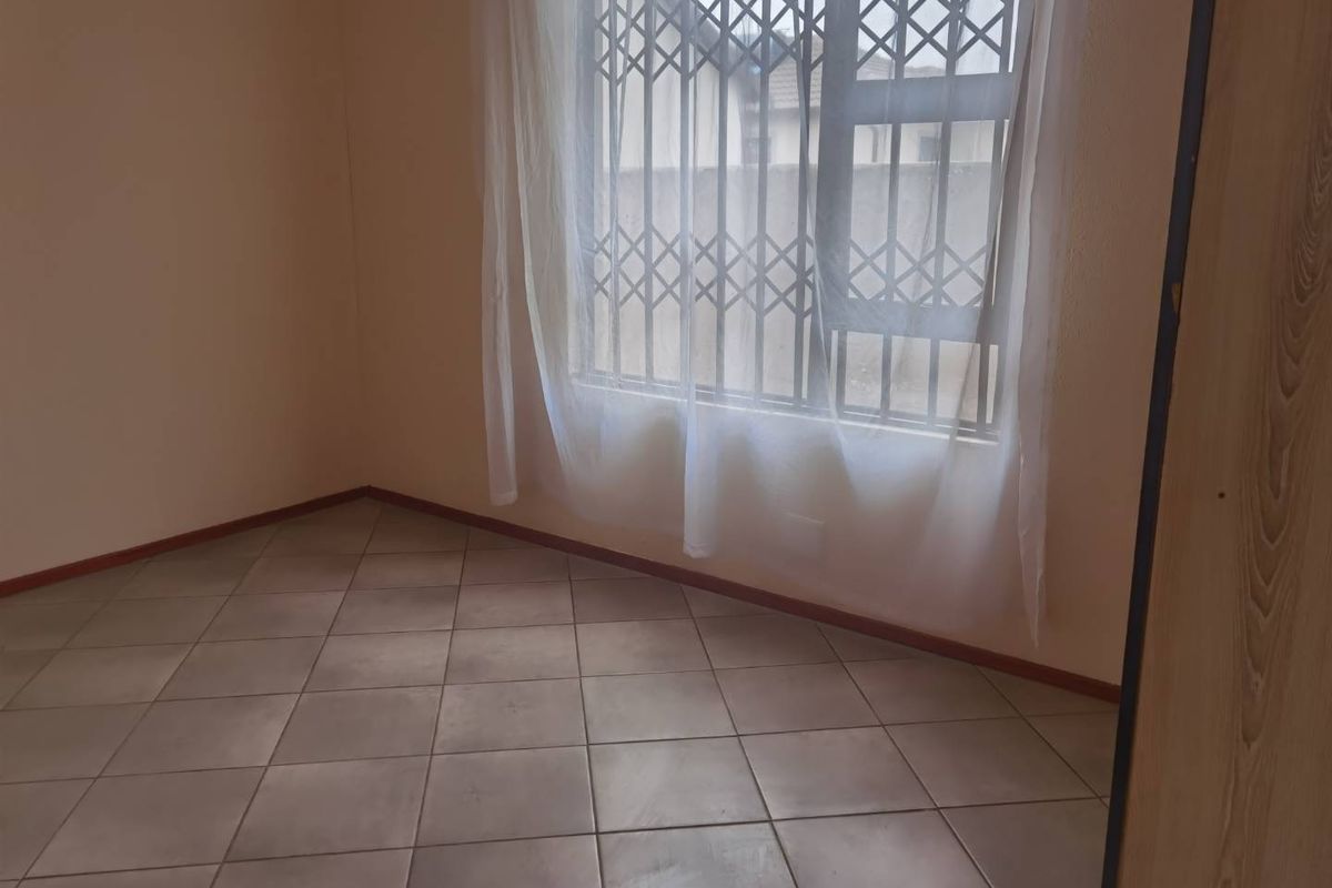 An empty bedroom featuring neutral tiled flooring and a window fitted with a security gate.