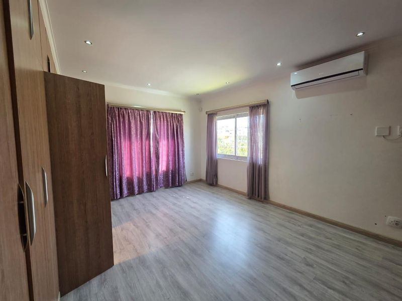 A spacious, empty bedroom featuring light-toned laminate flooring, built-in cupboards, recessed lighting, and a wall-mounted air conditioning unit.