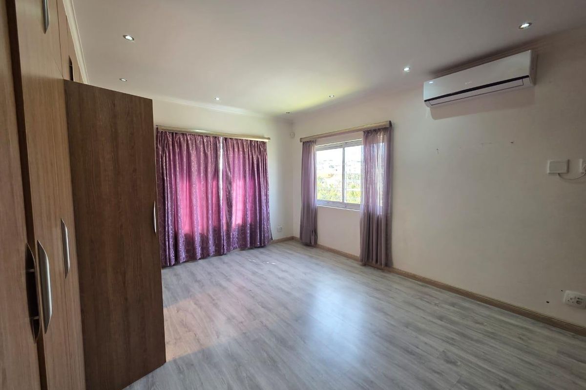 A spacious, empty bedroom featuring light-toned laminate flooring, built-in cupboards, recessed lighting, and a wall-mounted air conditioning unit.