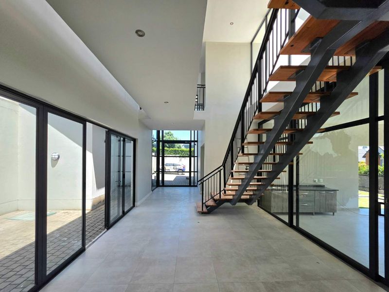 Spacious modern hallway featuring a striking open-tread staircase, large glass sliding doors, and high ceilings, creating a bright and airy architectural transition space.