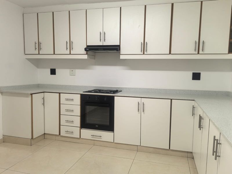 A clean, functional kitchen featuring white built-in cabinetry, speckled laminate countertops, a built-in oven with gas hob, and neutral tiled flooring.