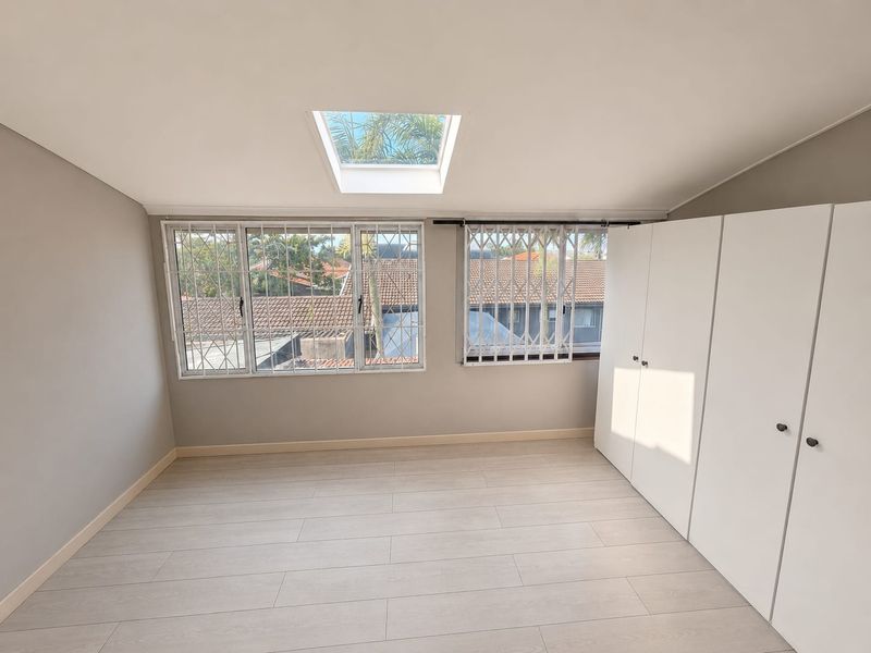 A bright, empty bedroom featuring modern laminate flooring, built-in cupboards, and a skylight, providing a clean and neutral space ready for personalization.