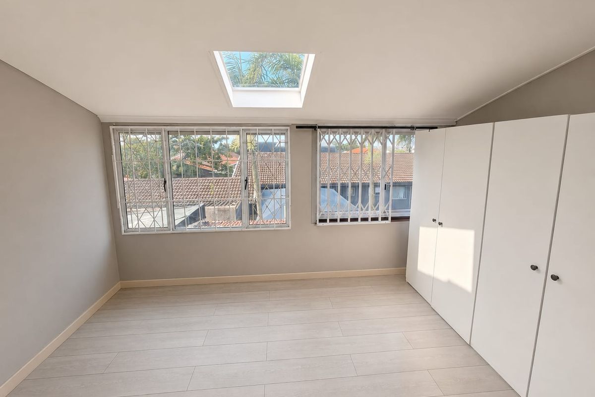 A bright, empty bedroom featuring modern laminate flooring, built-in cupboards, and a skylight, providing a clean and neutral space ready for personalization.
