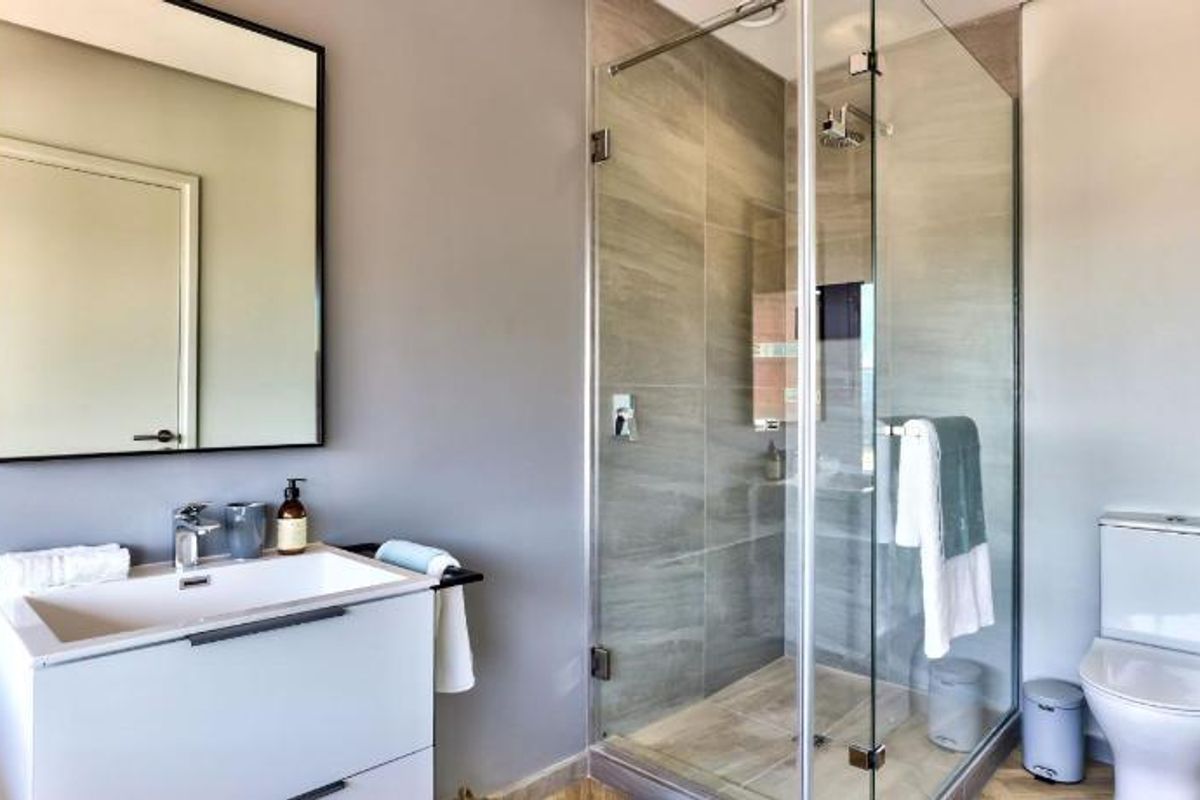 Modern bathroom featuring a sleek vanity with basin, a glass-enclosed shower with tiled walls, and a contemporary toilet.